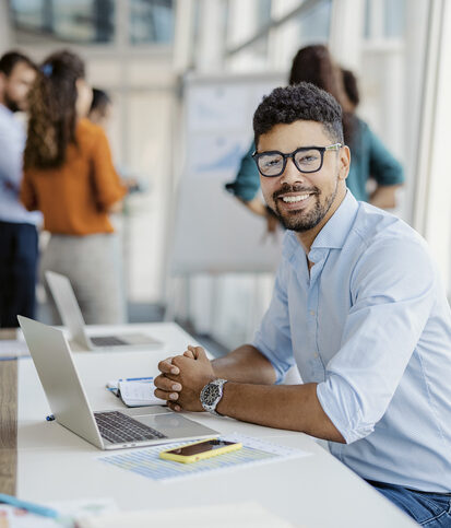 Portrait of young man entrepreneur looking at camera in the office with colleagues in the background.