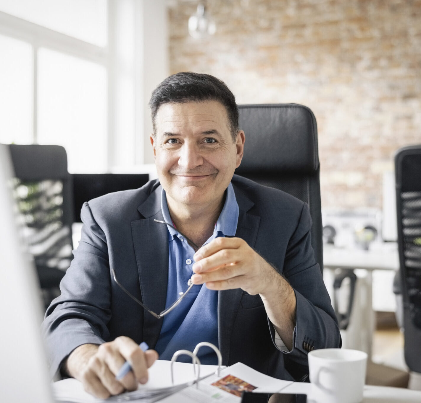 Portrait of a happy mid adult businessman sitting at office. Mature businessman in suit working at his desk in office.