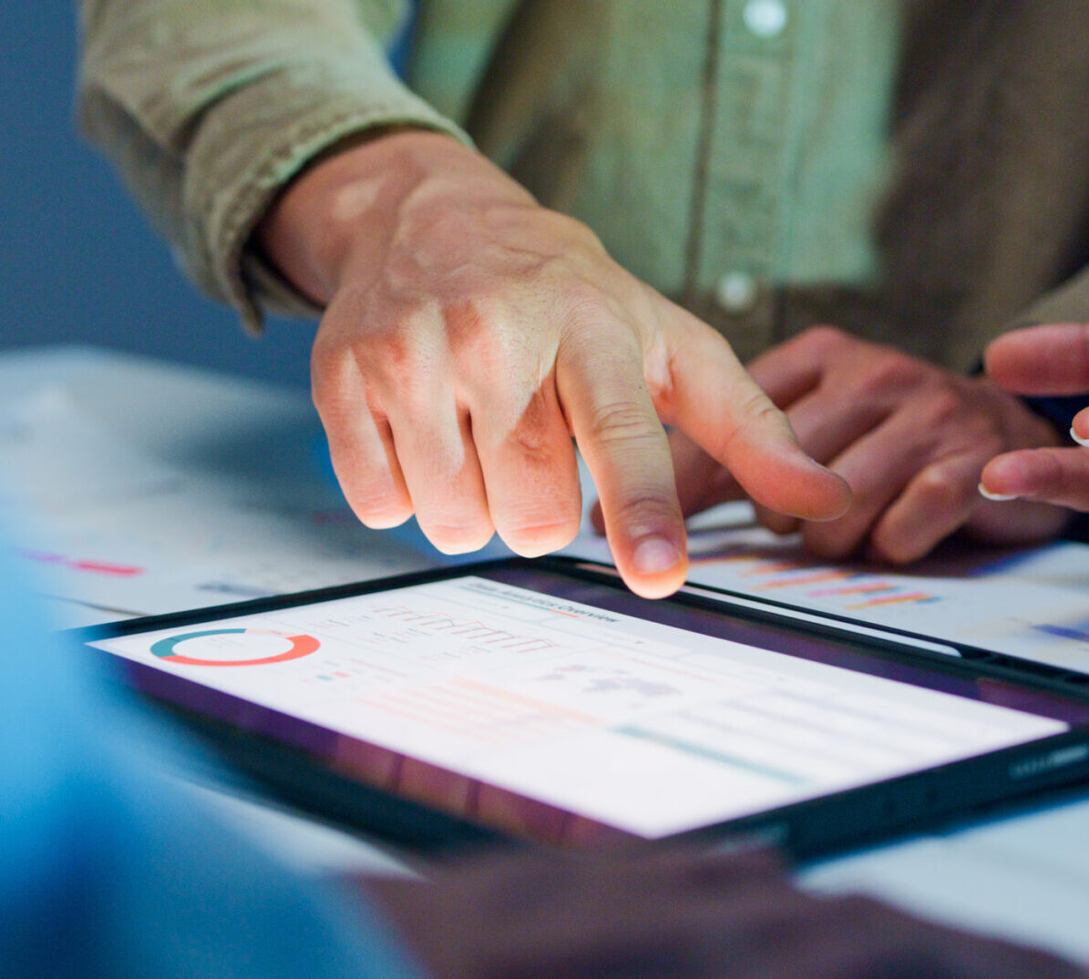 Close-up group analyzing financial reports and charts on digital tablet surrounded by documents and graphs during strategic meeting at office night. F